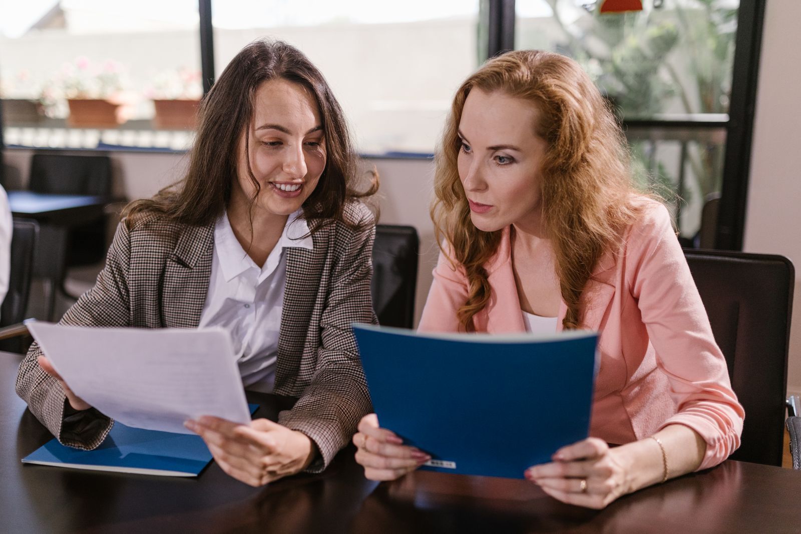 Two businesswomen sitting at a table, smiling and reviewing paperwork together.